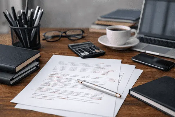 Professional office desk with edited documents, laptop, calculator, notebooks, and pen representing business report and professional document editing