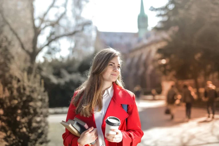 Female university student holding books and coffee while walking on campus